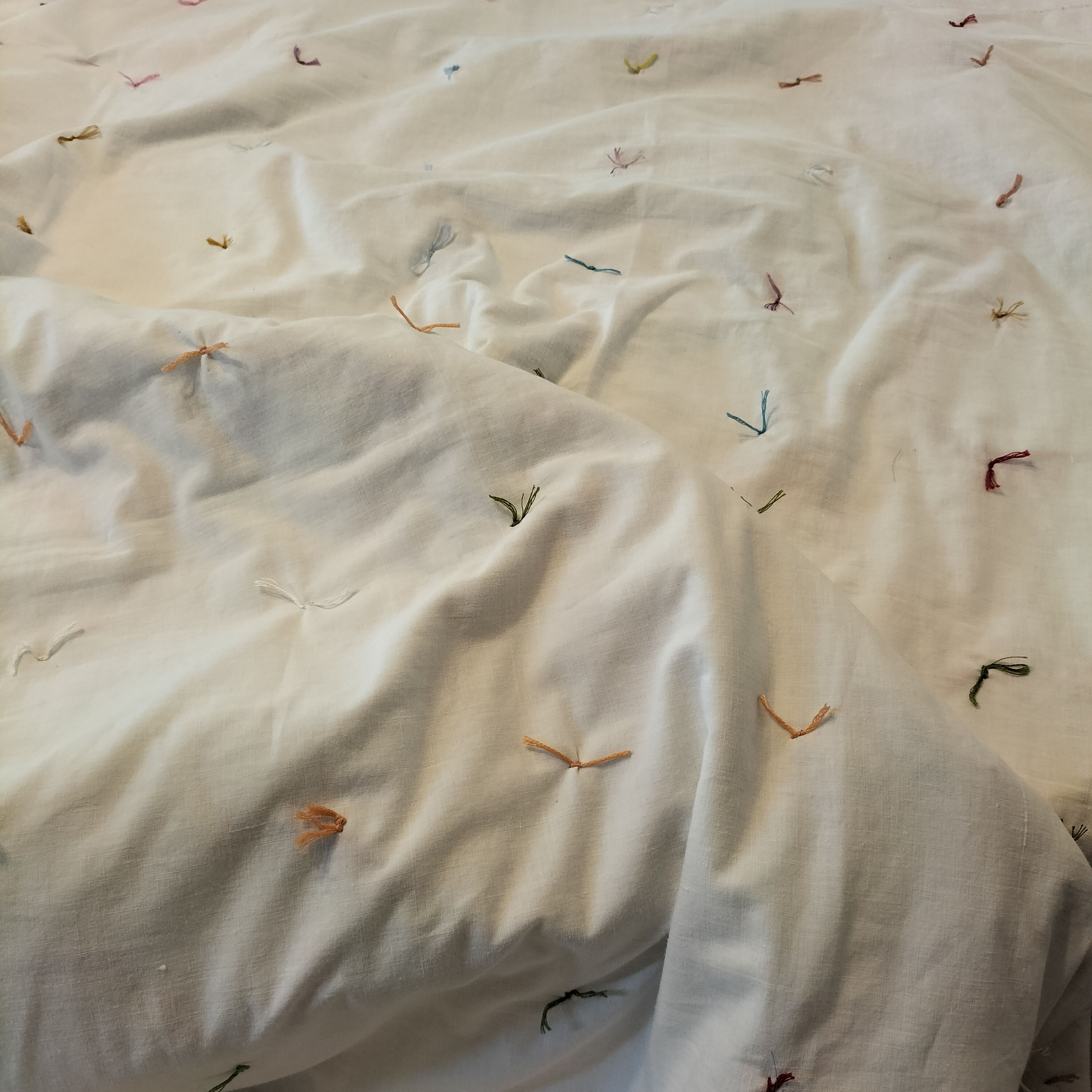 A white quilt back with multi-coloured knots in a grid format.