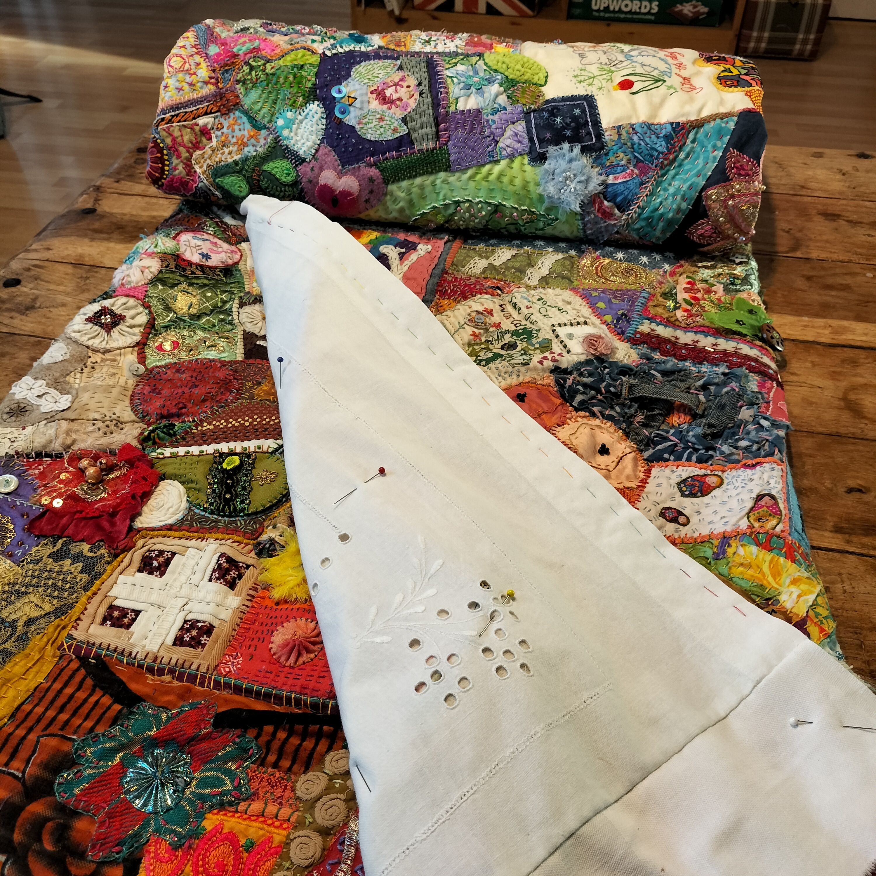 A partially-rolled patchwork quilt with the corner turned back to show the backing pinned in place.