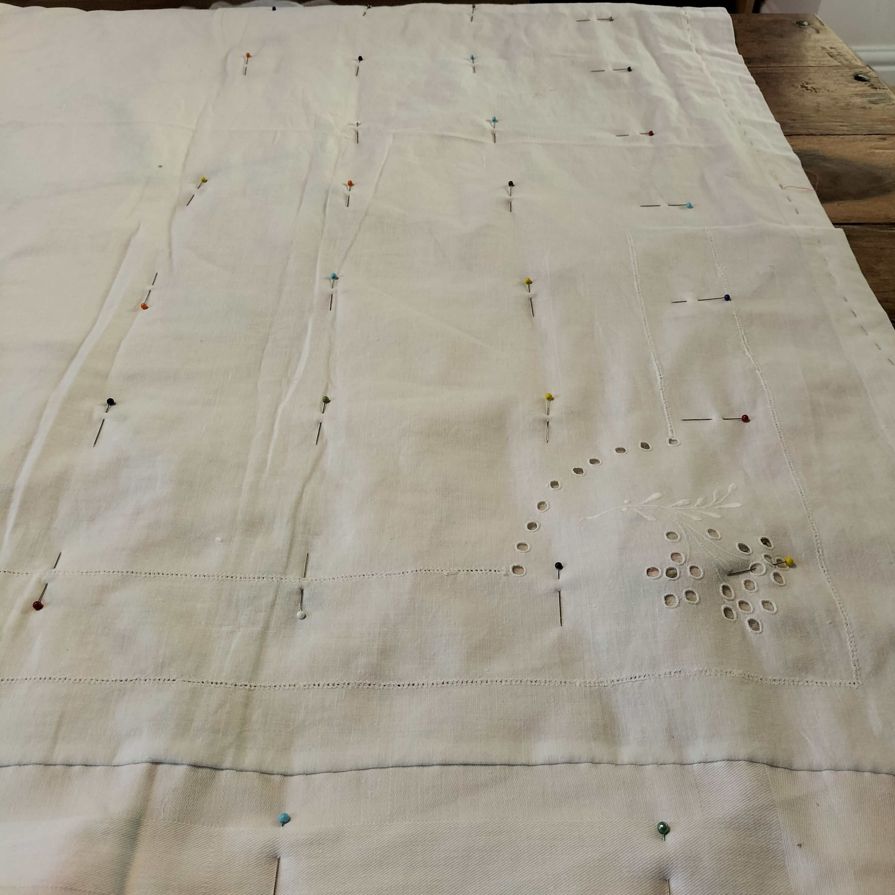 The white cotton backing of a quilt with a grid marked out with pins.