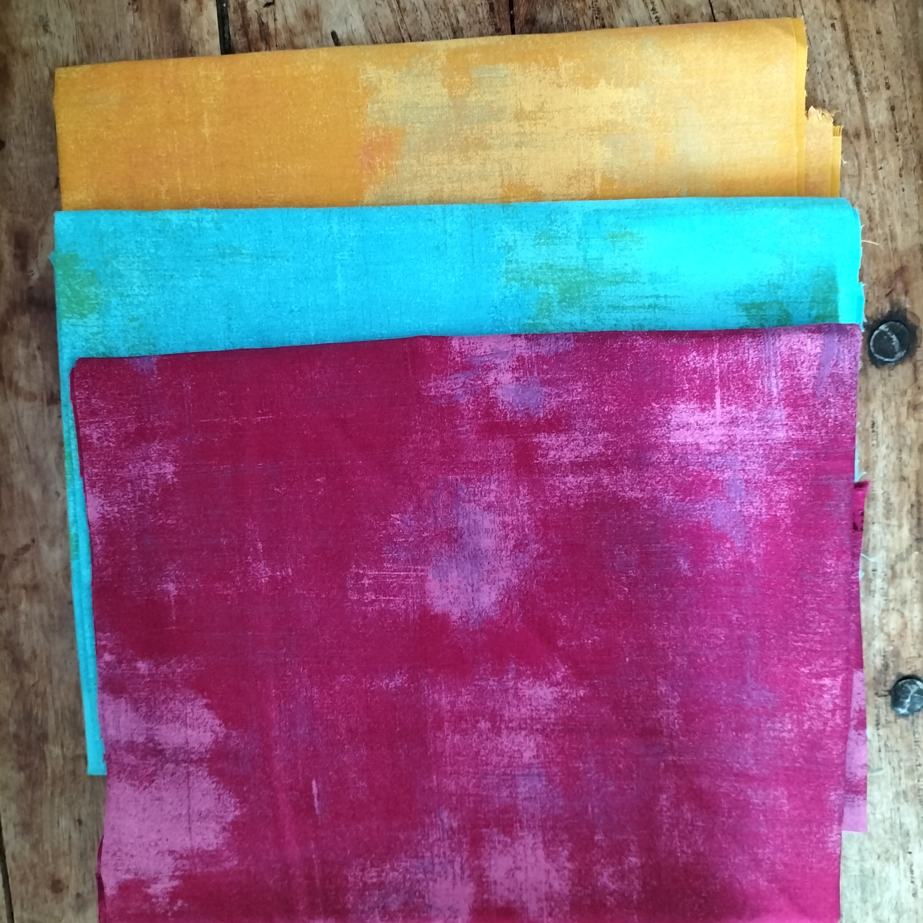 Three folded pieces of fabric in yellow, blue and deep pink.