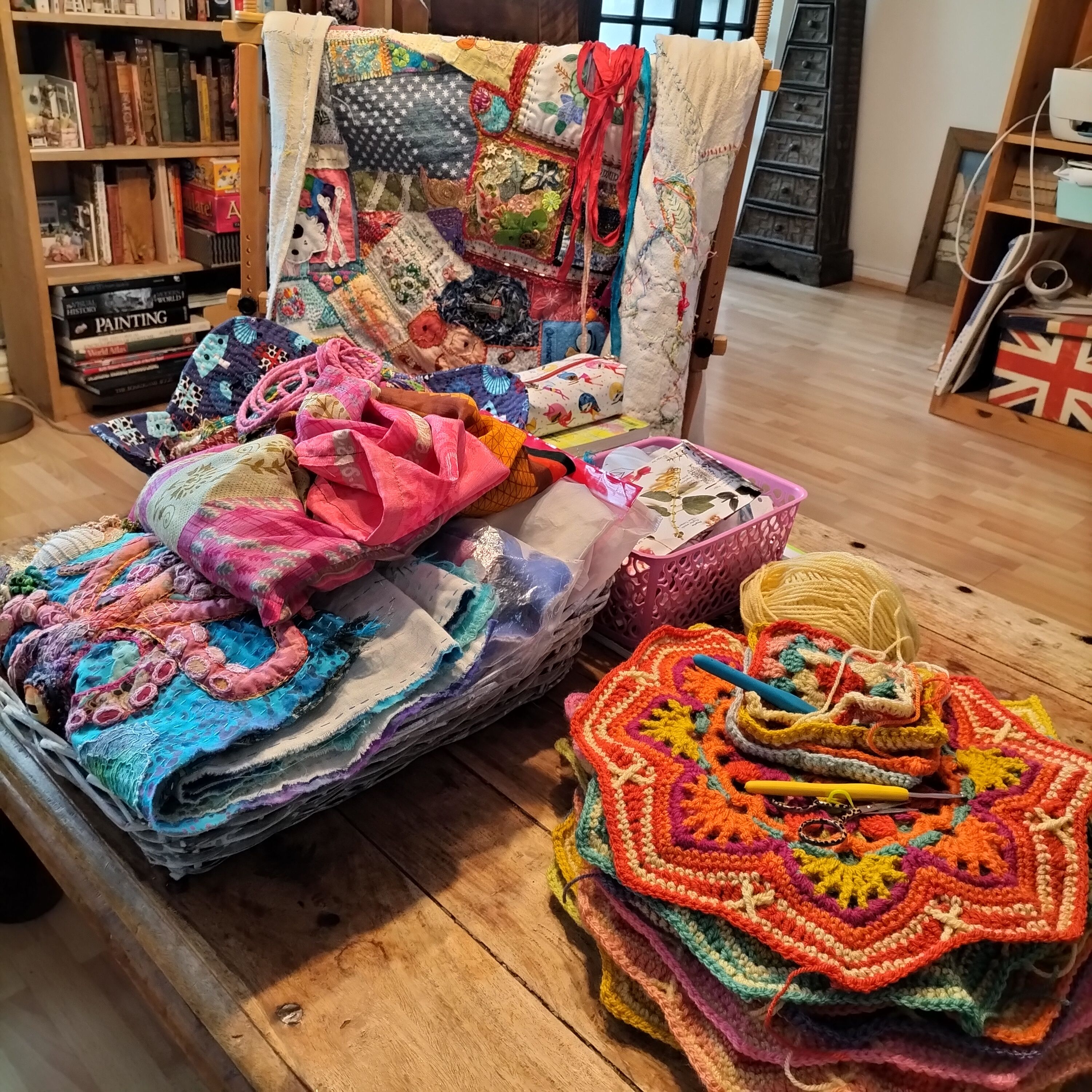 A sitting room scene, with various textile crafts piled on a large coffee table.