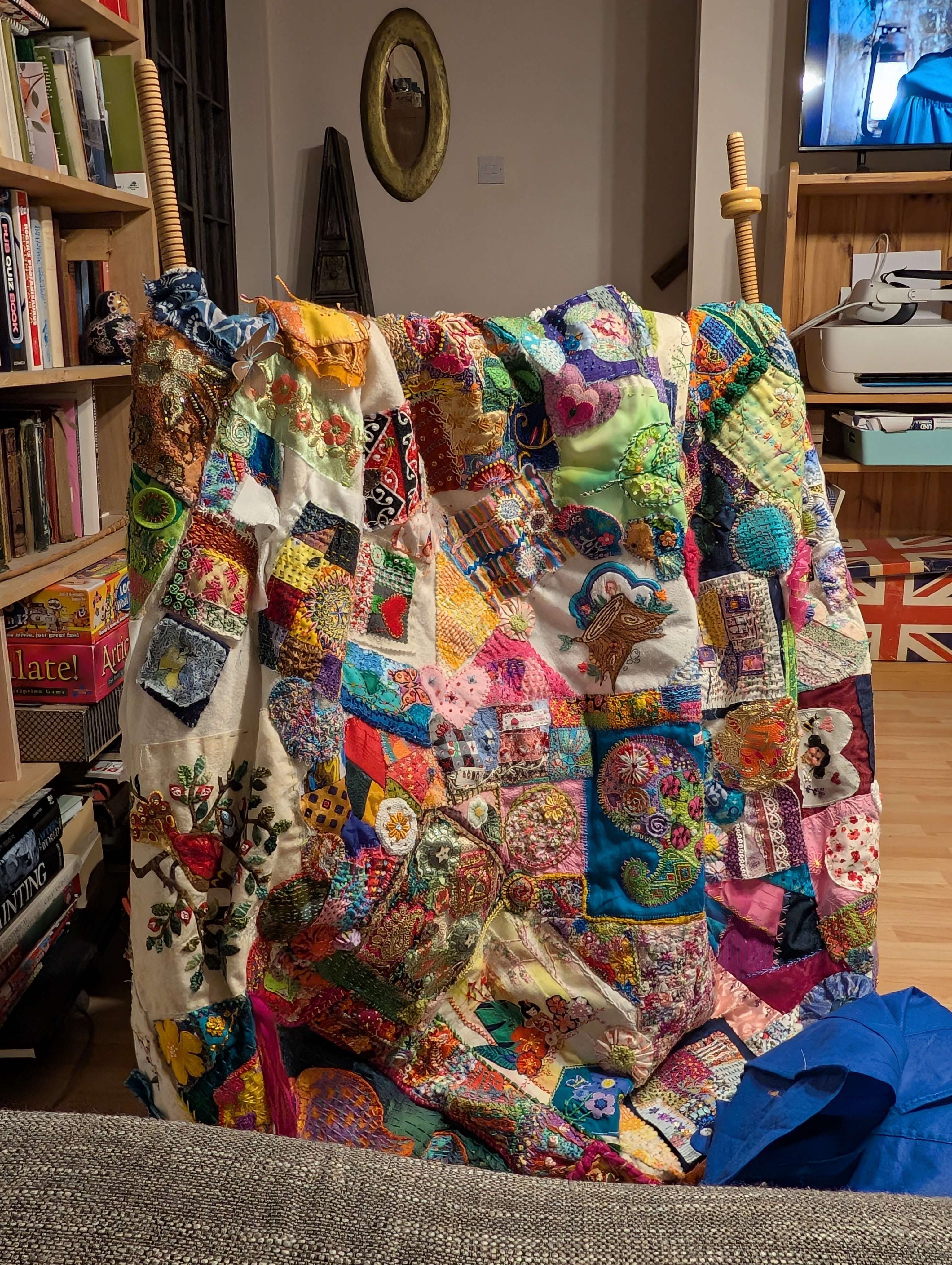 A crazy patchwork quilt draped over an embroidery frame in front of a sofa
