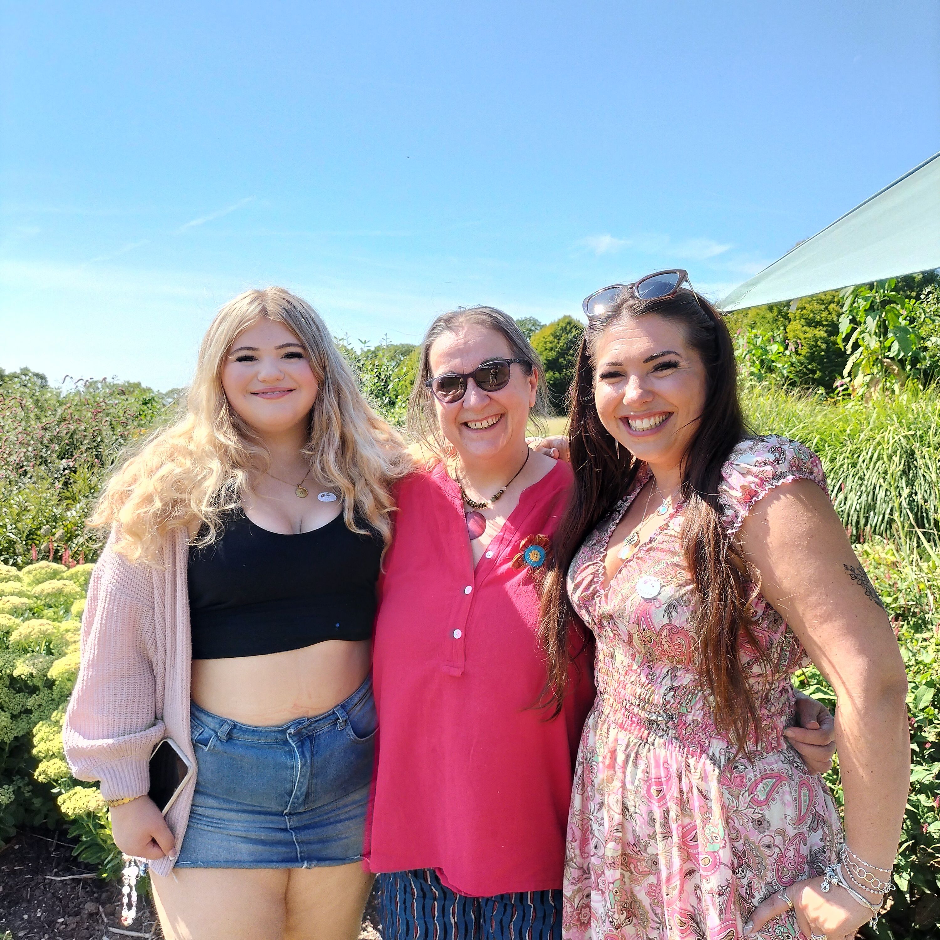 Three smiling people standing with their arms around each other in a summery garden setting