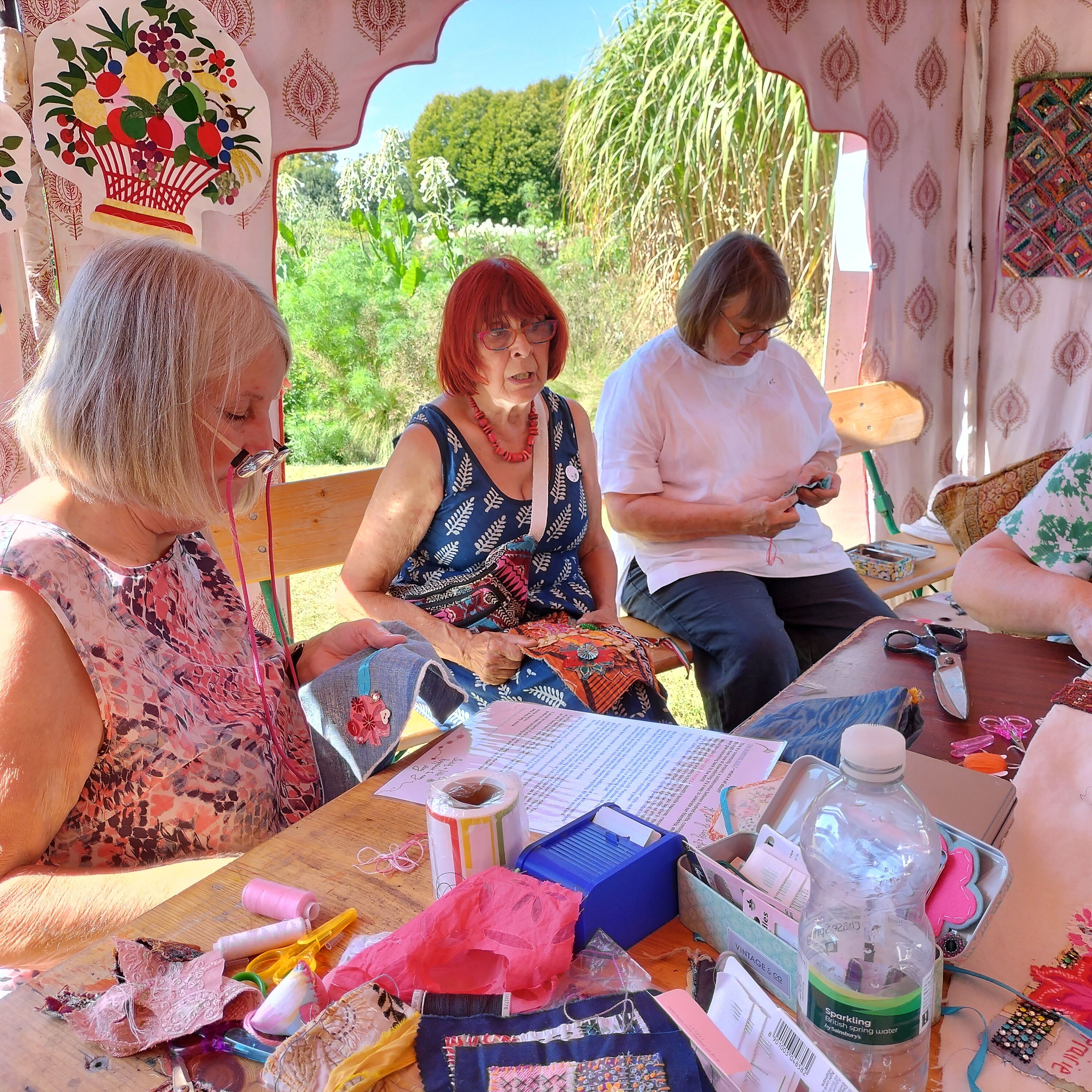 Three ladies sitting at a table stitching on pieces of fabric