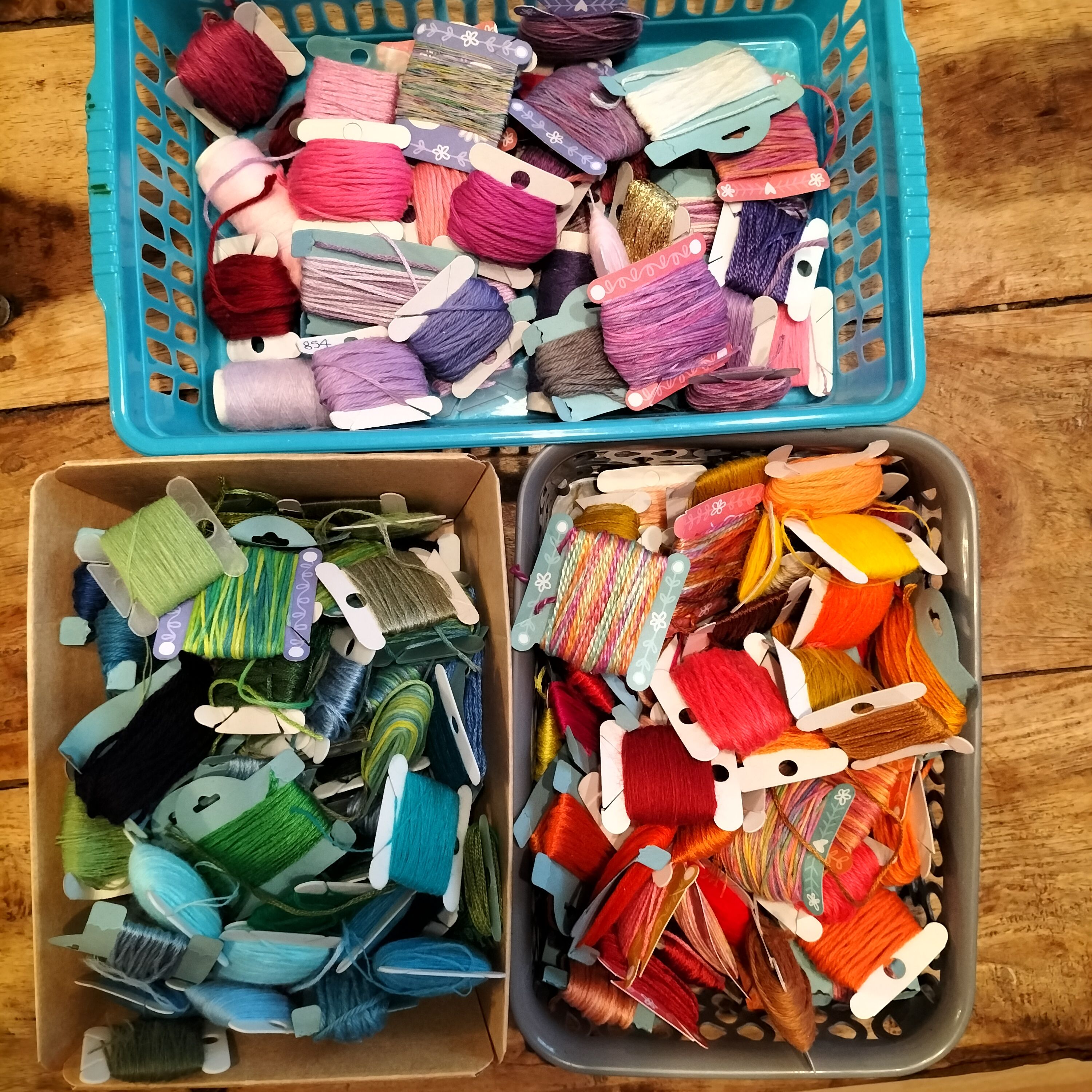 Three baskets holding a variety of threads wound onto bobbins and arranged in colour families