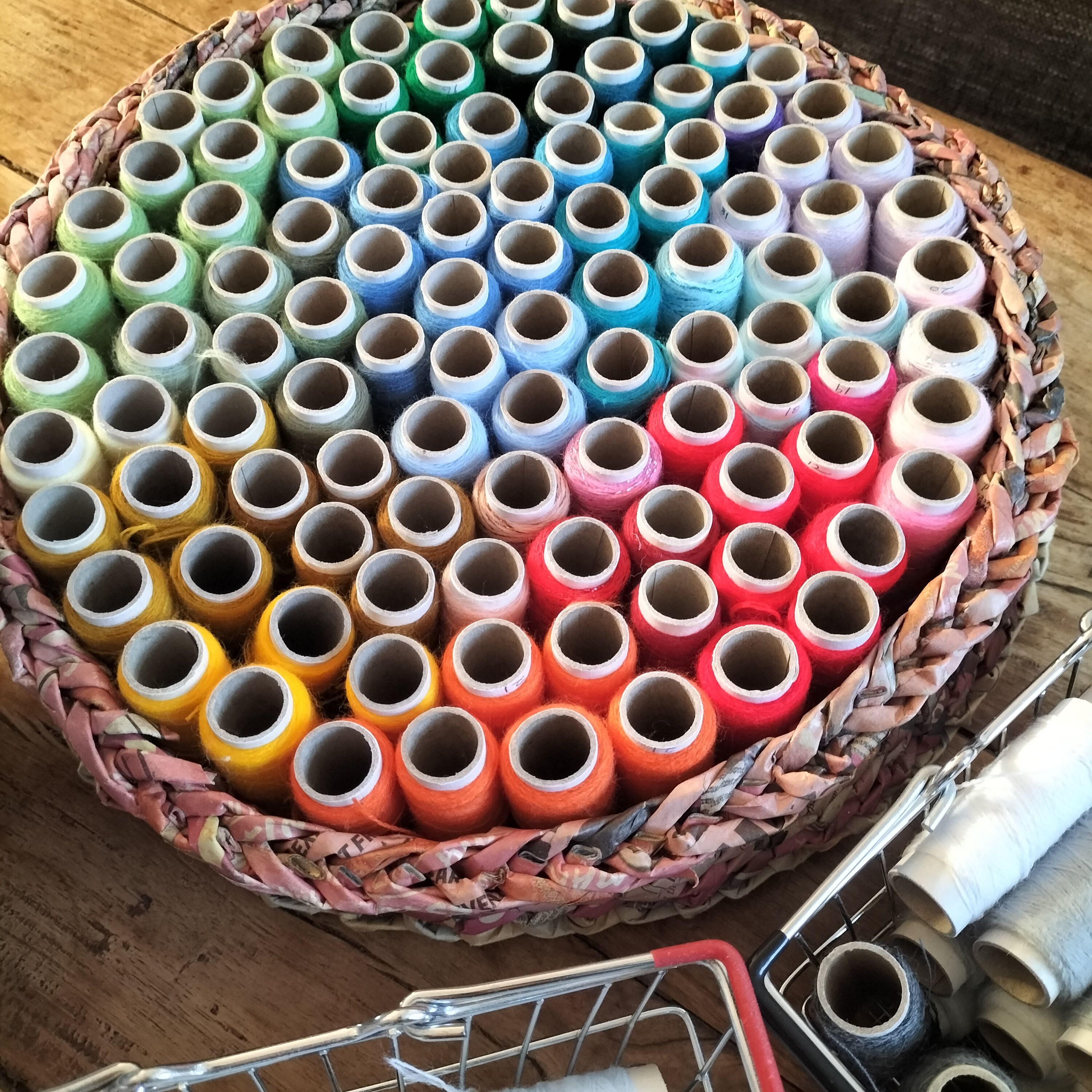 A circular basket holding colourful reels of thread arranged in rainbow order