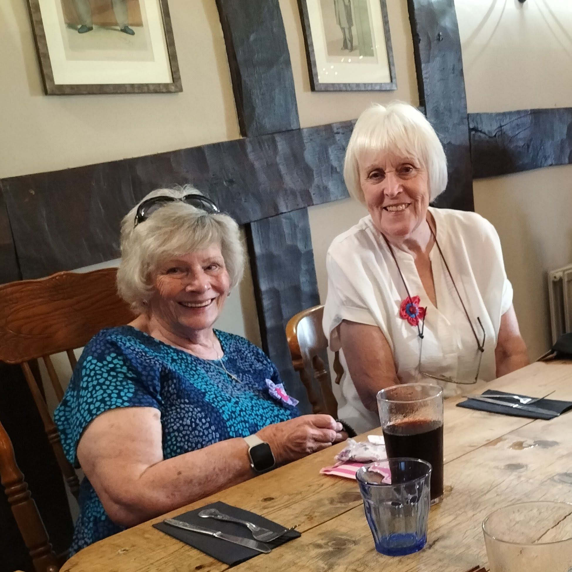 Two smiling ladies dressed in summery tops sitting at a table in a pub