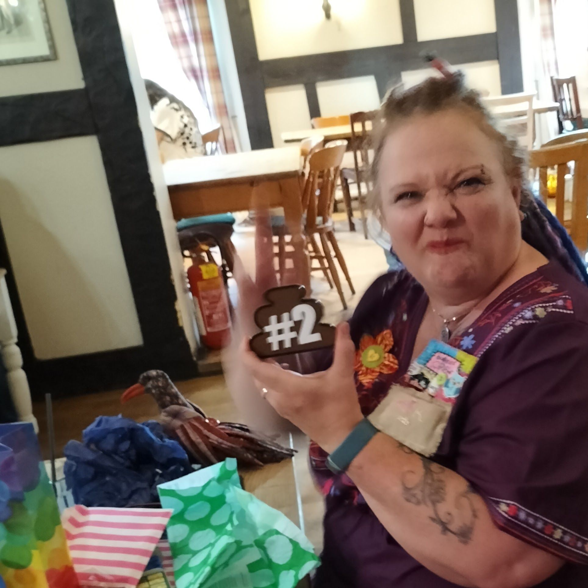 A grimacing woman holding up a brown poo emoji badge with #2 on it