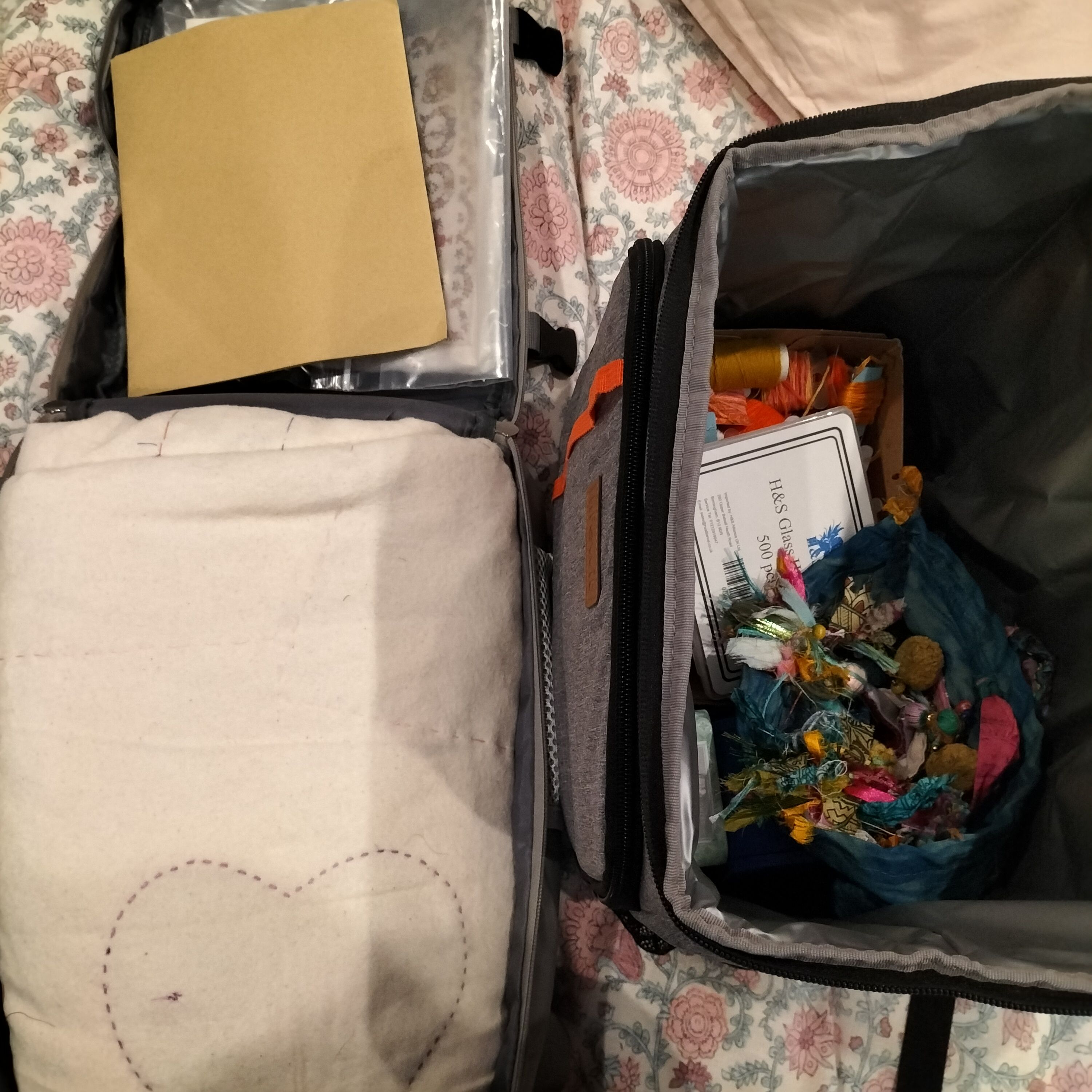 A quilt folded into a suitcase and another open bag with threads and fabrics